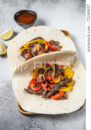 Fajitas with beef meat stripes, colored bell pepper and onions, served with tortillas and salsa. White background. Top view Fajitas with beef meat stripes, colored bell pepper and onions, served with tortillas and salsa. White background. Top view 75298857