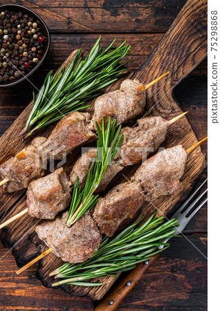 Shish kebab on skewers with herbs on a wooden board. Dark wooden background. Top view 75298868