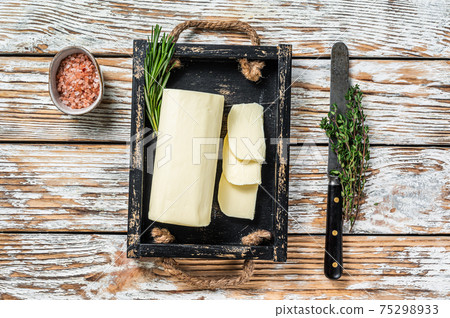 Butter Margarine block in a wooden tray with herbs. White wooden background. Top view Butter Margarine block in a wooden tray with herbs. White wooden background. Top view 75298933