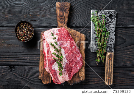 Fresh Raw Round roast beef meat cut on a butcher cutting board with cleaver. Black wooden background. Top view Fresh Raw Round roast beef meat cut on a butcher cutting board with cleaver. Black wooden background. Top view 75299123