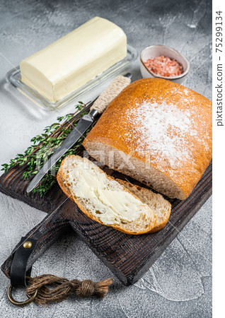 Butter block and sliced toasts of bread on a wooden board with herbs. White background. Top view Butter block and sliced toasts of bread on a wooden board with herbs. White background. Top view 75299134