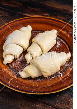 Raw uncooked homemade croissant on a rustic plate. Dark Wooden background. Top view Raw uncooked homemade croissant on a rustic plate. Dark Wooden background. Top view 75299148
