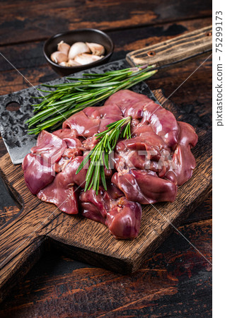 Raw liver chicken offals meat on a wooden cutting board with butcher cleaver. Dark wooden background. Top view 75299173