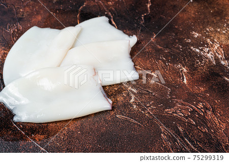 Raw Squid or Calamari tubes on a kitchen table. Dark background. Top view. Copy space 75299319
