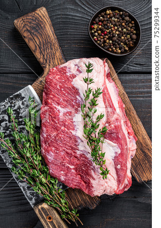 Fresh Raw Round roast beef meat cut on a butcher cutting board with cleaver. Black wooden background. Top view 75299344