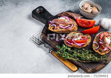 Toasts with olive oil, herbs, tomatoes and spicy anchovy fillets. White background. Top view. Copy space Toasts with olive oil, herbs, tomatoes and spicy anchovy fillets. White background. Top view. Copy space 75299401
