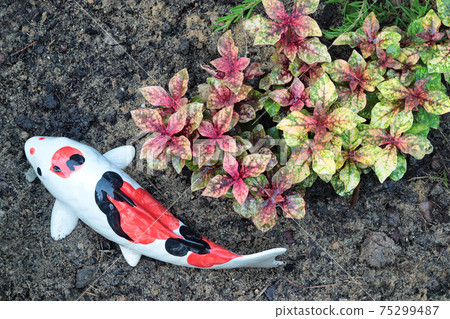 Statues of kraft fish on the ground lay beside multicoloured ornamental trees in garden park. 75299487