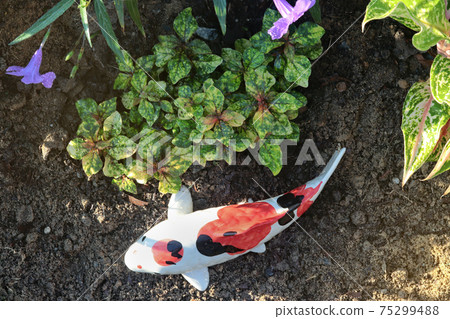 Statues of kraft fish on the ground lay beside multicoloured ornamental trees in garden park. 75299488