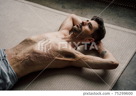 Naked man with scars at the skin after burn laying at the floor after exercises Naked man with scars at the skin after burn laying at the floor after exercises 75299600