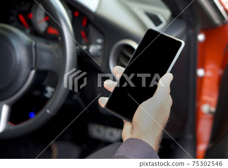 A blank screen mobile phone in the hand of a business man sitting in a sports car. 75302546