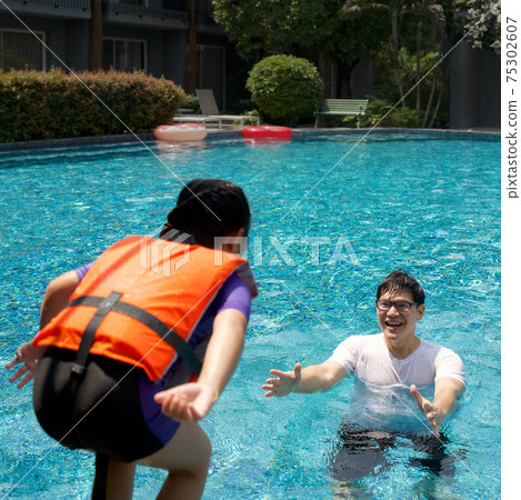 An Asian dad takes a vacation with his family in the pool, preparing to catch his daughter who will jump into the water. 75302607