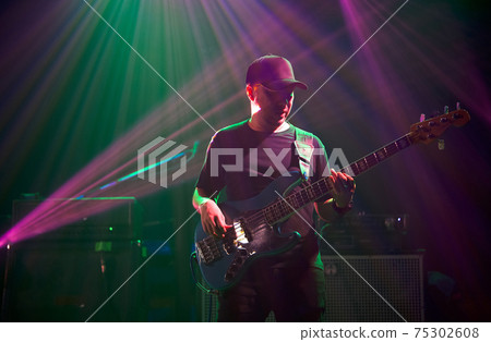 Asian bassist in black cap playing electric bass on stage. The atmosphere at night in the pub 75302608