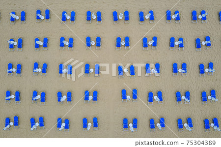 many white umbrellas and blue lounge chairs.  75304389