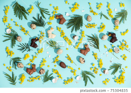 Happy Easter. Yellow Mimosa flowers, Chocolate Easter Bunny and quail eggs on blue paper background, flat lay 75304835