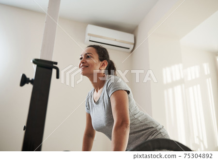 Determined young female deadlifting barbell in home gym 75304892