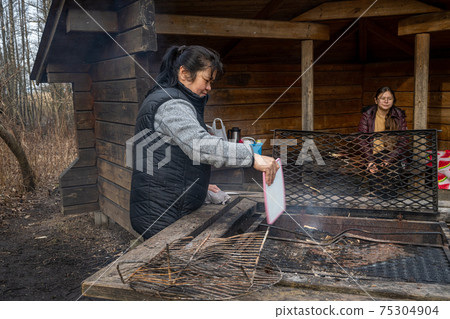 A middle-aged Asian woman cooking Souvlakia at a campsite fireplace. 75304904