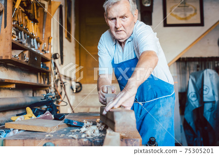Experienced master carpenter working with planer on wood 75305201