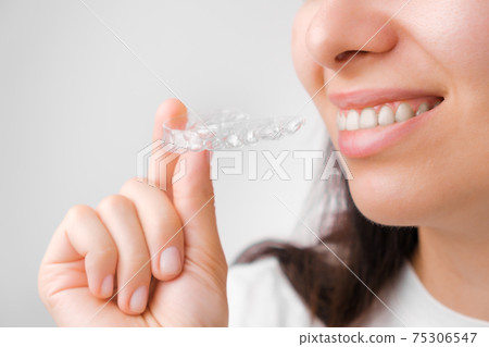 Close up of a young woman adjusting transparent aligners. Taking care of teeth. Orthodontic treatment for straightening and whitening teeth. Close up of a young woman adjusting transparent aligners. Taking care of teeth. Orthodontic treatment for straightening and whitening teeth. 75306547