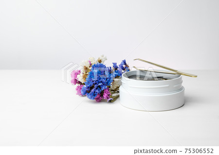 A white box with golden patches and tweezers on the white table with colorful flowers with copy space. Cosmetics product for skin care with anti-wrinkle effect. A white box with golden patches and tweezers on the white table with colorful flowers with copy space. Cosmetics product for skin care with anti-wrinkle effect. 75306552