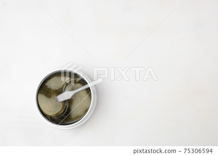 Top view on the plastic jar with golden eye patches and spatula isolated on the white background with copy space. 75306594