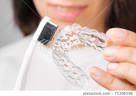Close up woman showing how to clean invisible removable braces or aligners using toothbrush. Close up woman showing how to clean invisible removable braces or aligners using toothbrush. 75306596