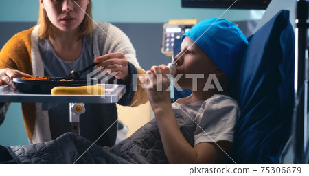 Woman feeding boy in hospital ward 75306879