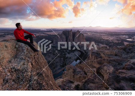 Man standing on top of a mountain is enjoying a beautiful landscape 75306909