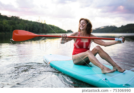 Senior woman paddleboarding on lake in summer. Copy space. Senior woman paddleboarding on lake in summer. Copy space. 75306990