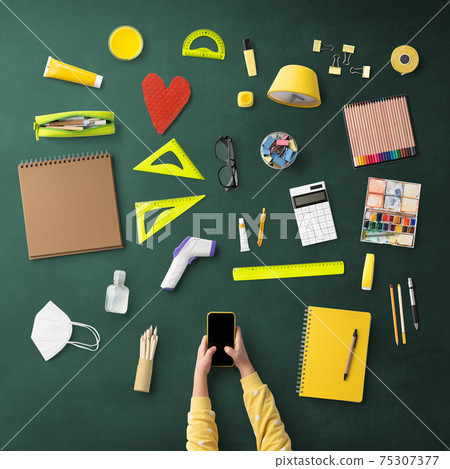 Flat lay top view of child with smartphone and school supplies, distance learning and coronavirus concept. Flat lay top view of child with smartphone and school supplies, distance learning and coronavirus concept. 75307377