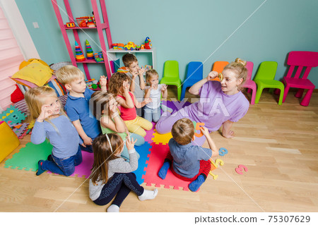 Preschool teacher teaching group of children, sitting on a floor 75307629