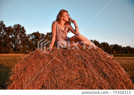 Portrait of young sexy woman with red hair on the haystack in morning sunlight, countryside. Beautiful woman in a dress sits on a haystack. Cottagecore Portrait of young sexy woman with red hair on the haystack in morning sunlight, countryside. Beautiful woman in a dress sits on a haystack. Cottagecore 75308313