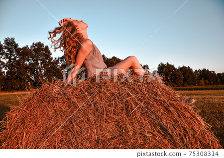 Portrait of young sexy woman with red hair on the haystack in morning sunlight, countryside. Beautiful woman in a dress sits on a haystack. Cottagecore Portrait of young sexy woman with red hair on the haystack in morning sunlight, countryside. Beautiful woman in a dress sits on a haystack. Cottagecore 75308314