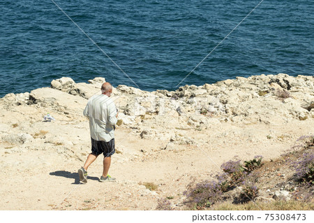 Tourist walks along the sandy path, mountain hiking. Blue sea on background 75308473