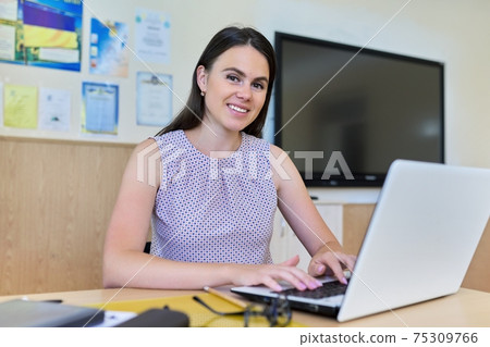 Portrait of young woman teacher working with laptop sitting in classroom 75309766