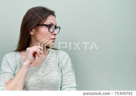 Portrait of alone sad mature woman with glasses on green background Portrait of alone sad mature woman with glasses on green background 75309791