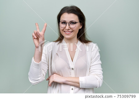 Happy mature confident woman showing victory symbol with hand gesture Happy mature confident woman showing victory symbol with hand gesture 75309799