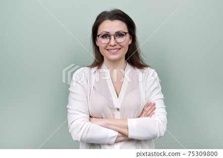 Middle aged smiling happy woman in glasses with crossed arms over green background Middle aged smiling happy woman in glasses with crossed arms over green background 75309800