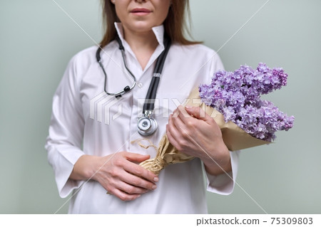 Bouquet of lilac flowers in the hands of female doctor with stethoscope 75309803