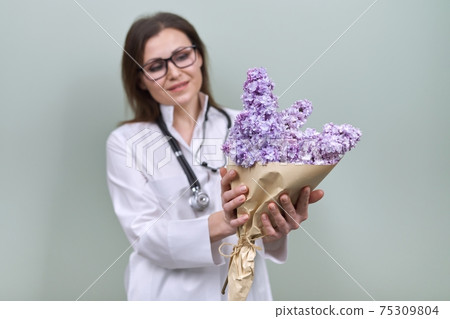 Bouquet of lilac flowers in the hands of female doctor with stethoscope Bouquet of lilac flowers in the hands of female doctor with stethoscope 75309804