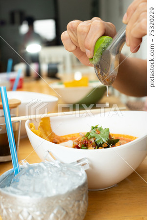 Asian Woman hand squeezing half of lemon lime on Spicy Noodle Soup Asian Woman hand squeezing half of lemon lime on Spicy Noodle Soup 75320229