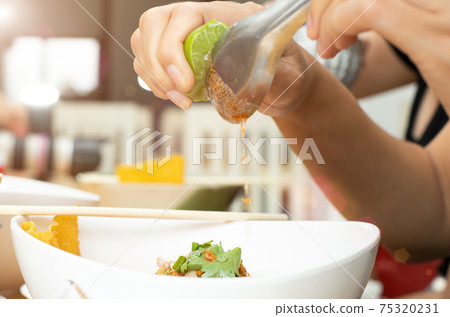 Asian Woman hand squeezing half of lemon lime on Spicy Noodle Soup Asian Woman hand squeezing half of lemon lime on Spicy Noodle Soup 75320231
