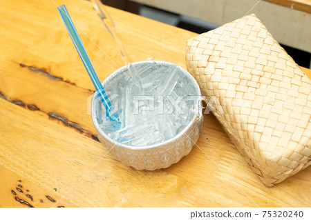 Pour Water on Ice in silver cup on wooden table with straw 75320240
