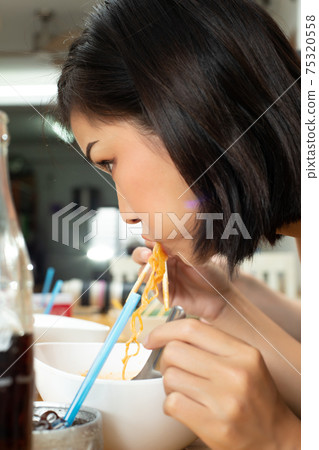 Woman eats spicy hot tomyum noodle soup and hanging on chopstick Woman eats spicy hot tomyum noodle soup and hanging on chopstick 75320558