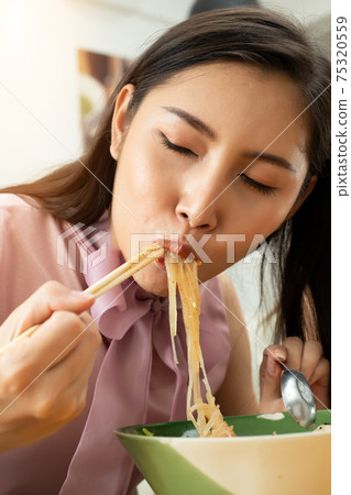 Woman eats spicy hot tomyum noodle soup and hanging on chopstick Woman eats spicy hot tomyum noodle soup and hanging on chopstick 75320559