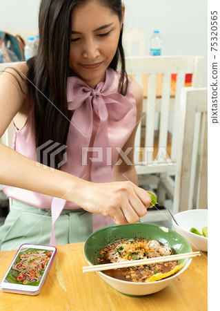 Asian Woman hand squeezing half of lemon lime on Spicy Noodle Soup 75320565