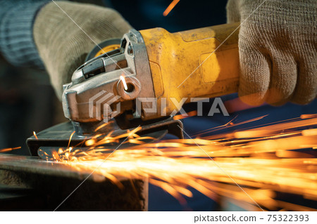 Locksmith in special clothes and goggles works in production. Metal processing with angle grinder. Sparks in metalworking 75322393