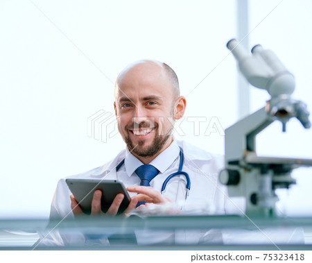 smiling researcher with a digital tablet sitting in front of a microscope smiling researcher with a digital tablet sitting in front of a microscope 75323418