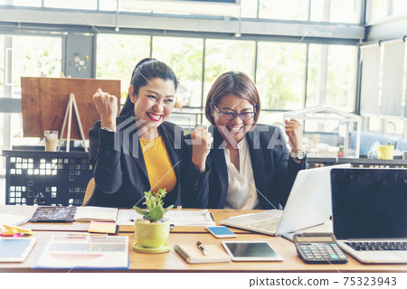 Happy success business woman partner working together in company office corporate executive teamwork. Meeting Executive Asian business woman using laptop office desk with fist arm raised win happiness Happy success business woman partner working together in company office corporate executive teamwork. Meeting Executive Asian business woman using laptop office desk with fist arm raised win happiness 75323943