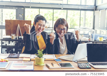 Happy success business woman partner working together in company office corporate executive teamwork. Meeting Executive Asian business woman using laptop office desk with fist arm raised win happiness Happy success business woman partner working together in company office corporate executive teamwork. Meeting Executive Asian business woman using laptop office desk with fist arm raised win happiness 75323945