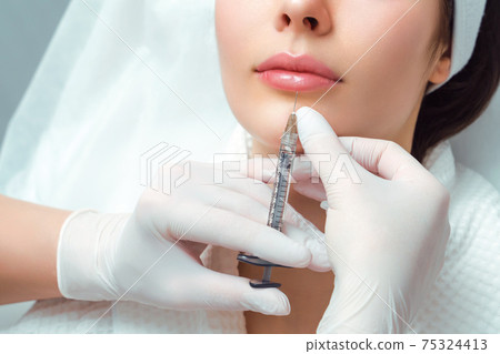 lip shape correction procedure in a cosmetology salon. The specialist makes an injection on the lips of the patient. Lip augmentation 75324413